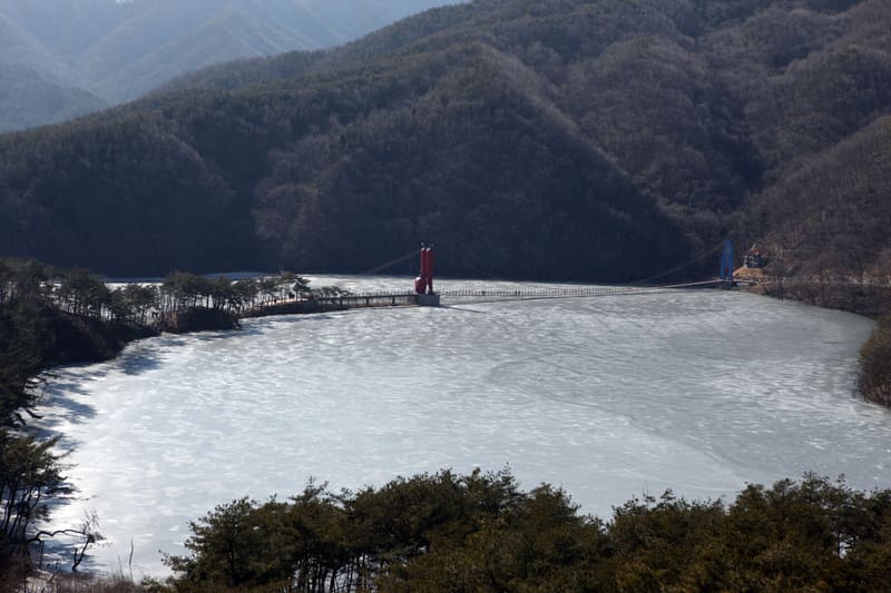 Cheonjangho Lake frozen over in winter, with its red-towered suspension bridge, near the Alps Village festival site
