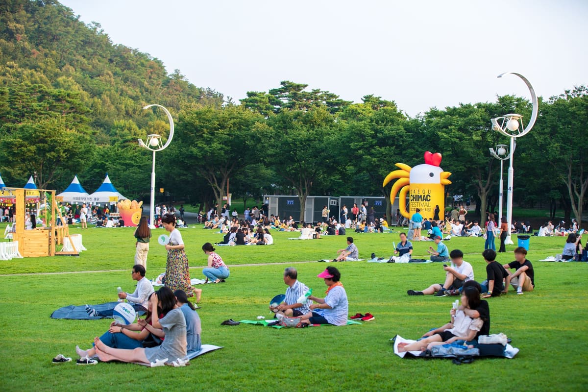 Picnickers on the lawn at Duryu Park on a summer afternoon, with the festival's giant inflatable chicken, at the 2018 festival