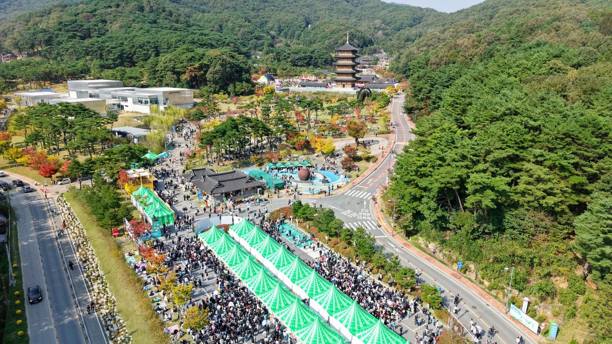 The festival grounds from above, with green booth tents along the road and the wooden pagoda beyond, 2025