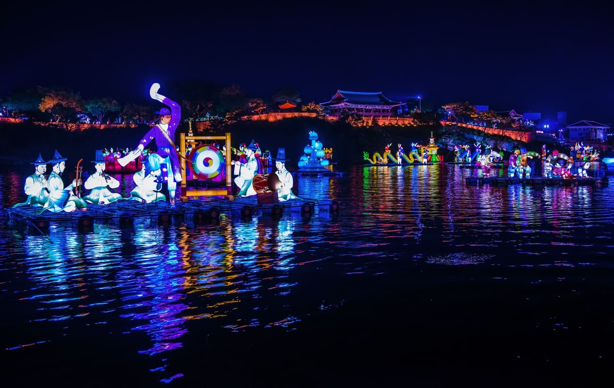 Lantern figures of musicians and a dancer on the Namgang River below the lit walls of Jinjuseong Fortress at night, 2014