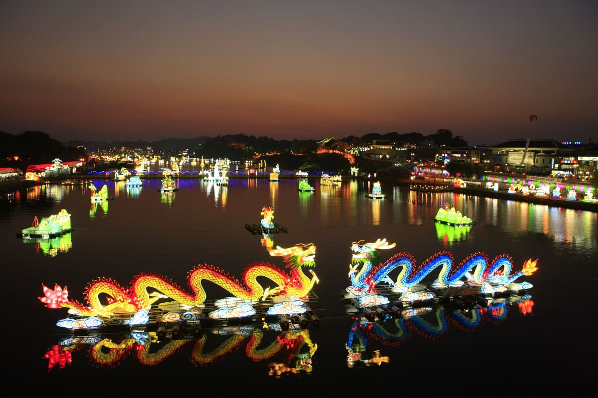 Dragon lanterns on the Namgang River at dusk, with the lit riverbank behind, 2011