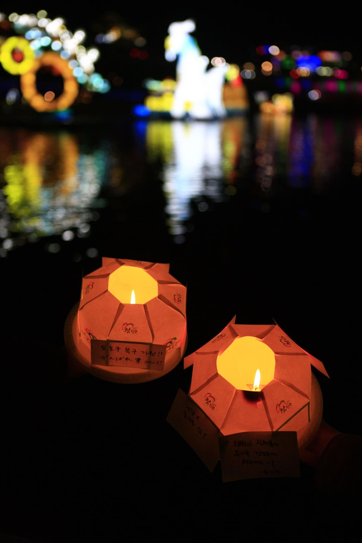 Small wish lanterns floating on the river at night, with the large lantern figures behind, 2011
