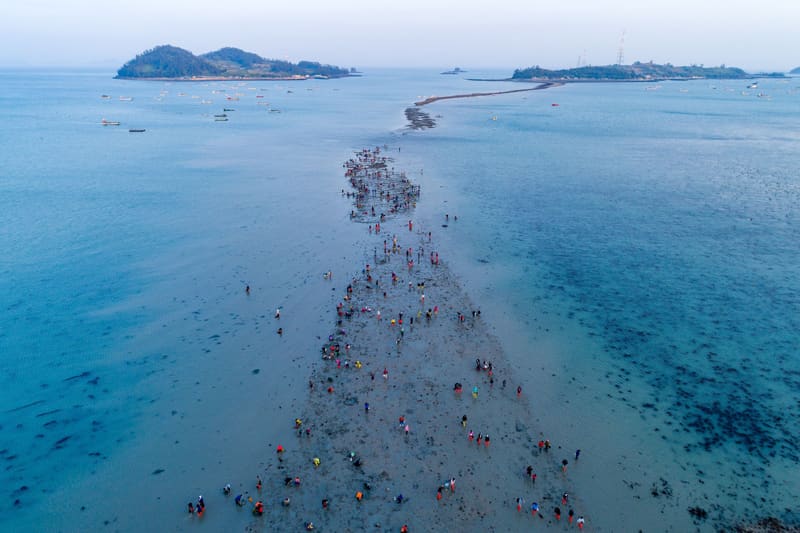 Crowds walking out along the sea road as the tide parts toward Modo island