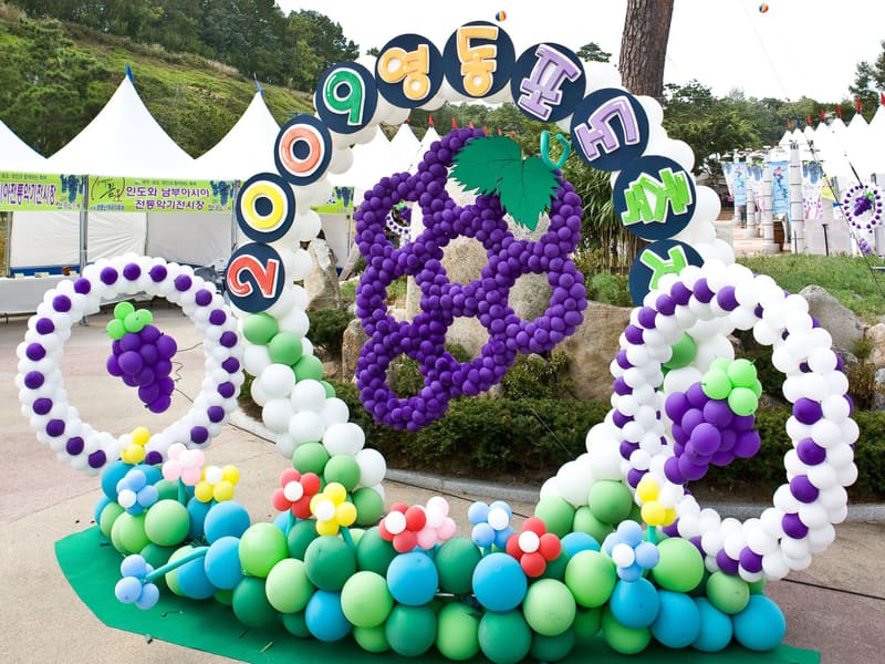 A balloon display of grape bunches spelling out the festival name at the 2009 Yeongdong Grape Festival, with booth tents behind
